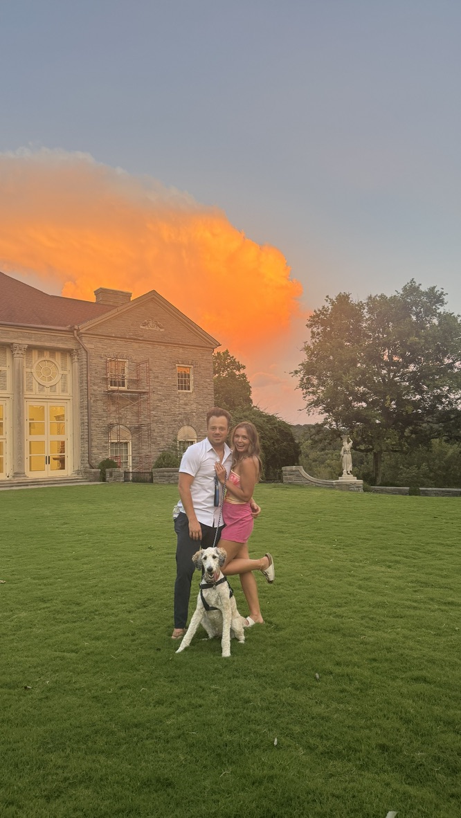 Drew and Katy with their dog under a vivid sunset sky