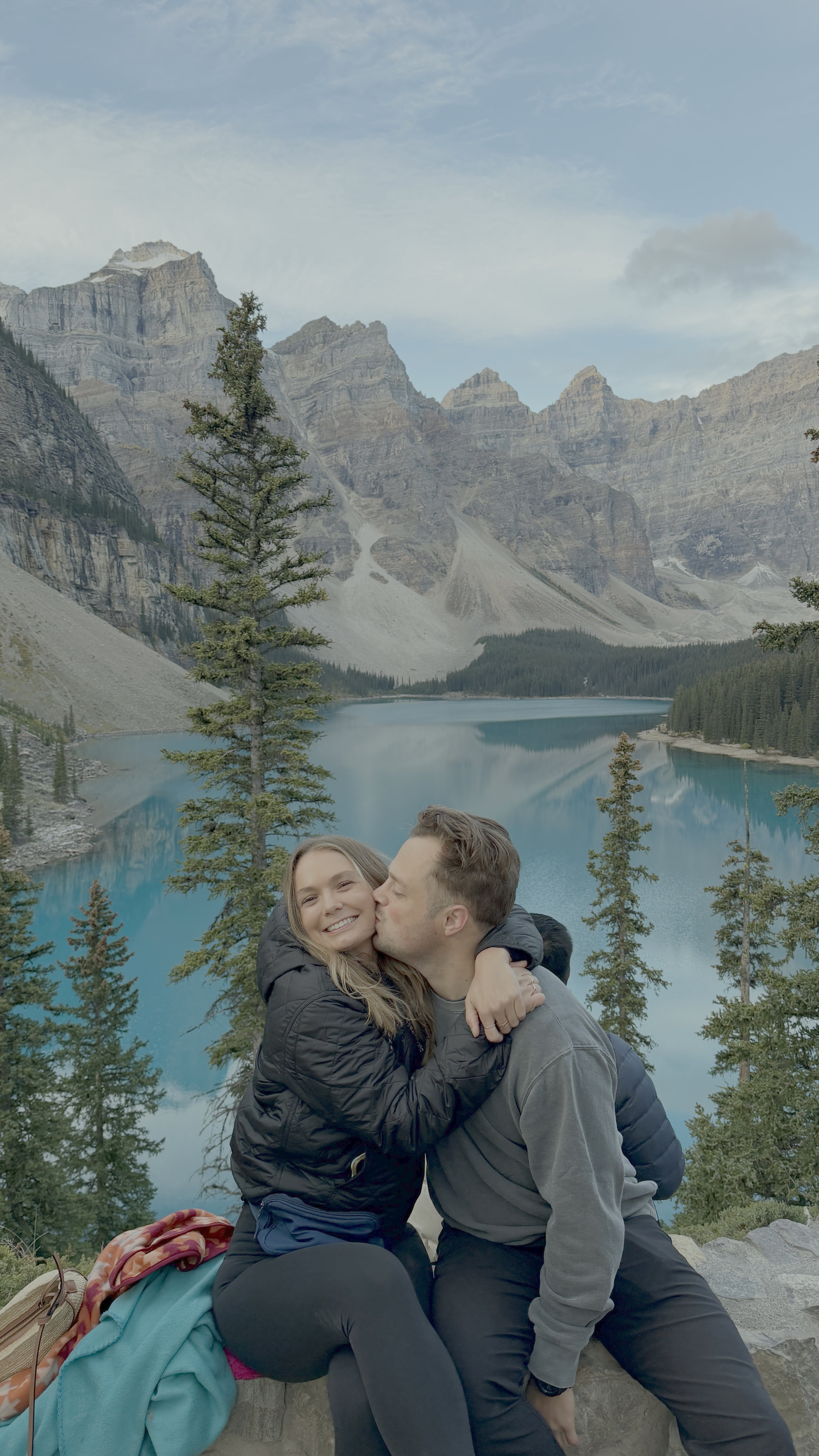 Katy and Drew embracing in front of a bright blue mountain lake